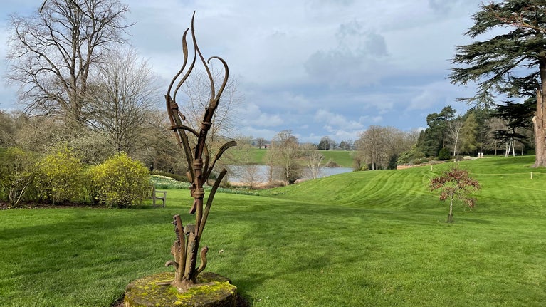 spring garden view with a curving metal sculpture in the foreground and a lake in the background